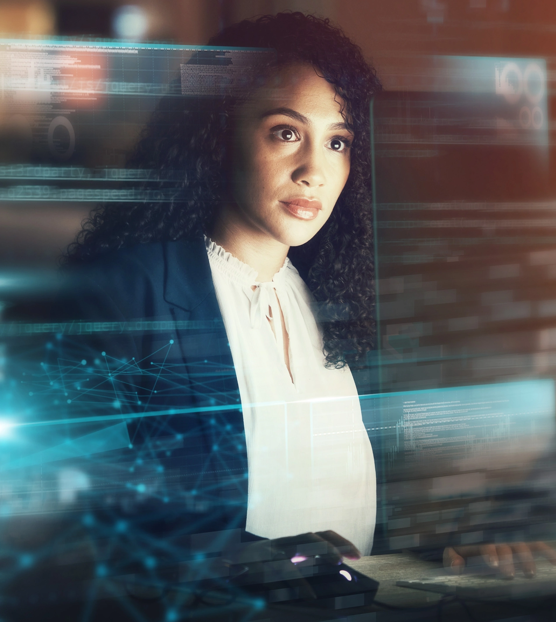 A woman smiles and makes a fist in celebration while looking at a tablet. She sits at a desk with a laptop, surrounded by digital code