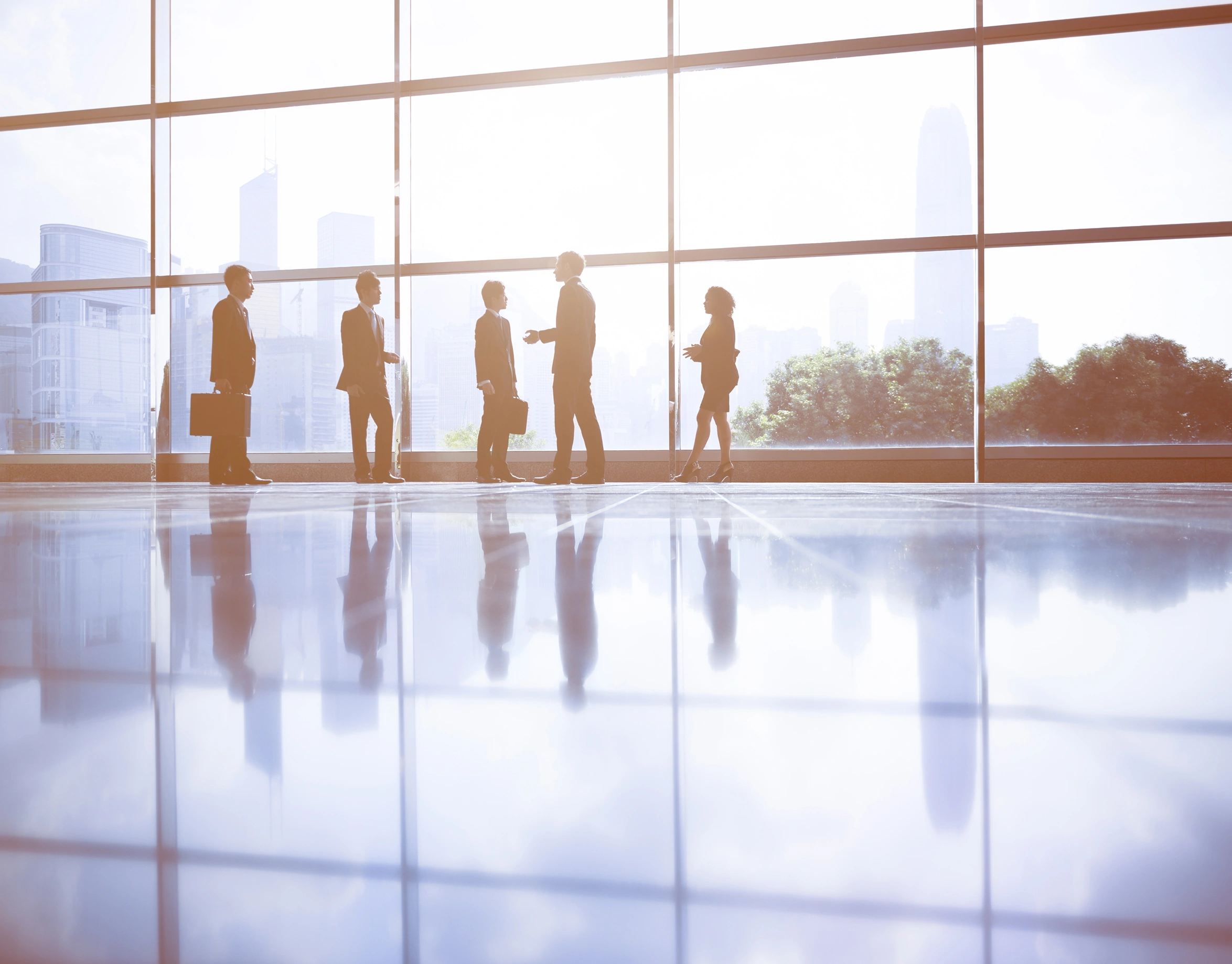 Silhouettes of five business people standing and talking in a modern office building with large windows, city skyline visible outside-mobile