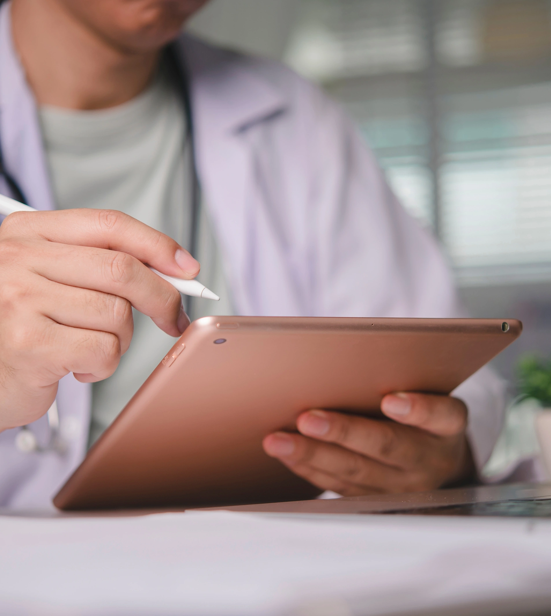 A medical professional in a lab coat uses a stylus to interact with a gold tablet.