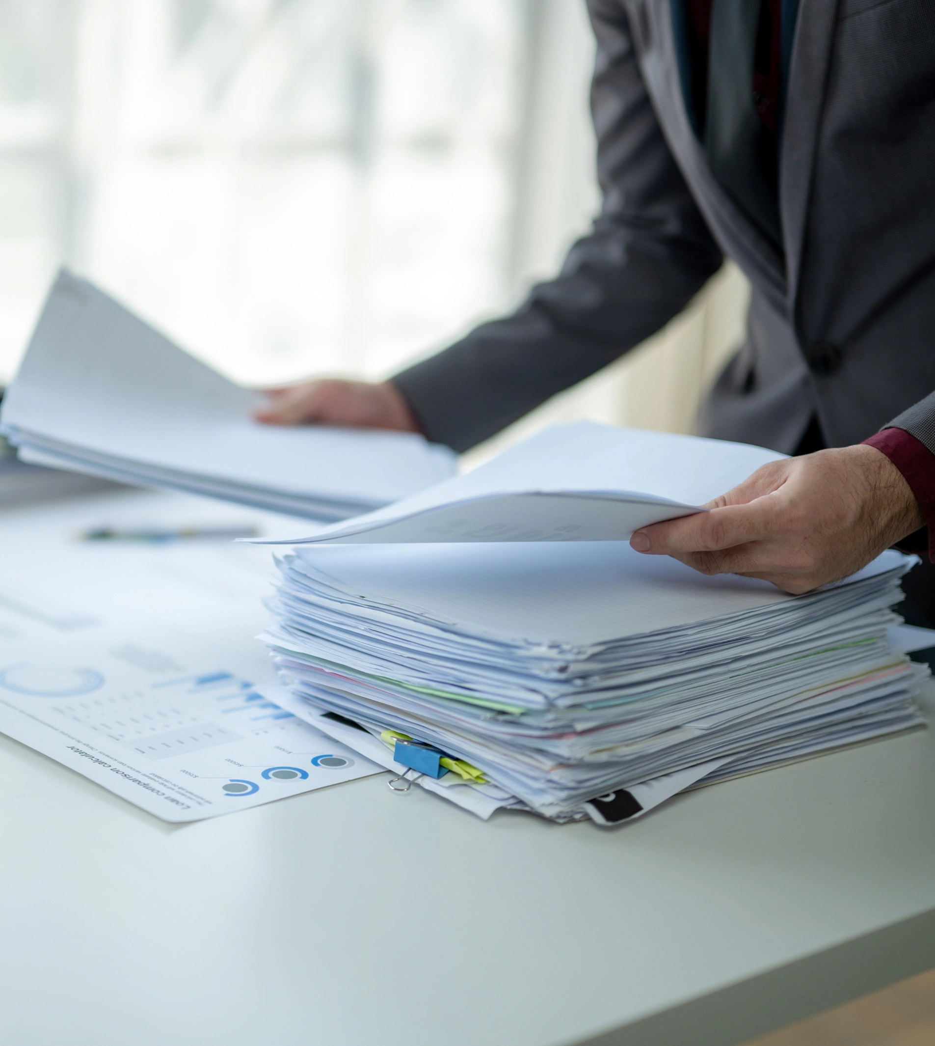 A person in a suit is handling a large stack of documents on a desk.