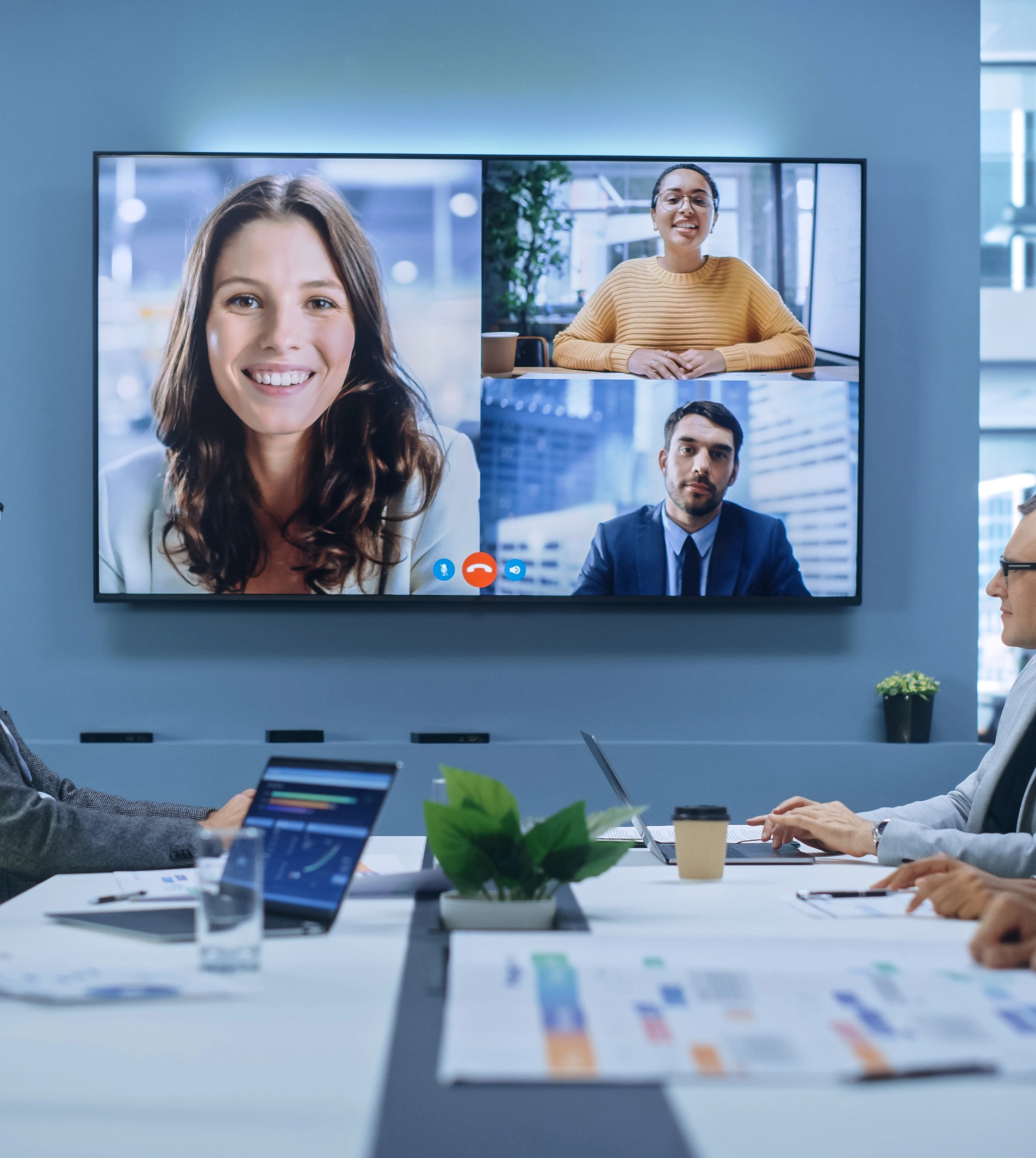 A team of four people participates in a video conference on a large screen in a modern office meeting room.