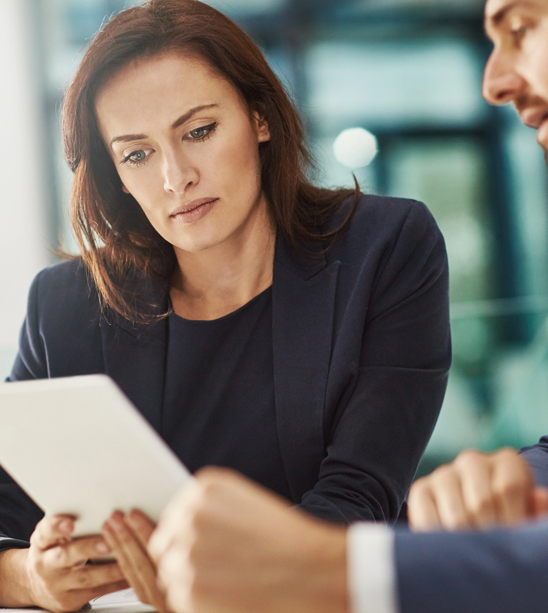 Two professionals, a woman and a man, review information on a tablet computer in a bright, modern office setting.